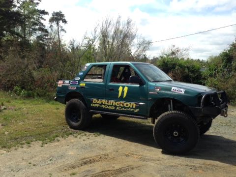 1999 Isuzu Vehicross - Modified green SUV with racing decals and large off-road tires, seen outdoors on a dirt track.