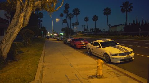1995 Ford Taurus - Several Ford Mustangs are parked along a sidewalk at night, illuminated by streetlights.