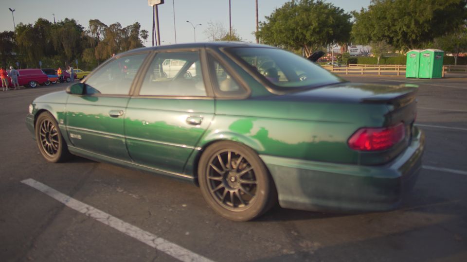 Green 1995 Ford Taurus sedan, rear quarter view, aftermarket wheels, spoiler