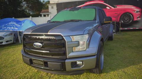 1995 Ford Taurus - A Ford F-150 pickup truck is parked on a lawn, with a red Ford Mustang on a trailer in the background.
