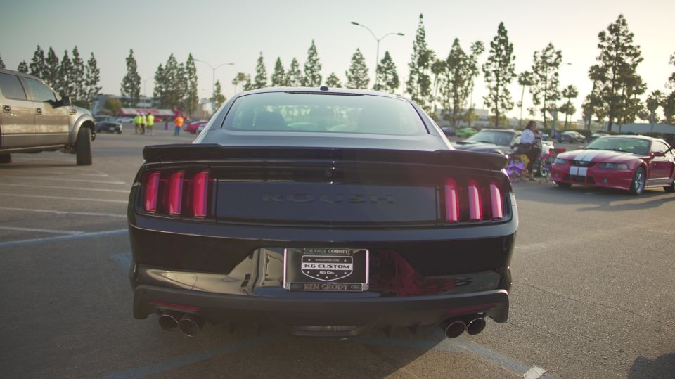 Black Ford Mustang rear view, Roush badging visible on trunk lid. Red Mustang in background