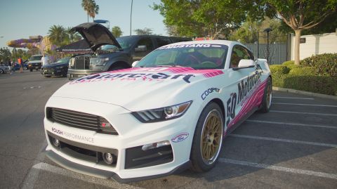 1995 Ford Taurus - A white Ford Mustang with racing decals and gold wheels is parked in a lot, with a black truck behind it.