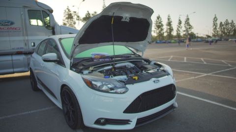 1995 Ford Taurus - A white Ford Focus ST is parked with its hood open, revealing the engine bay, next to a large semi-truck.