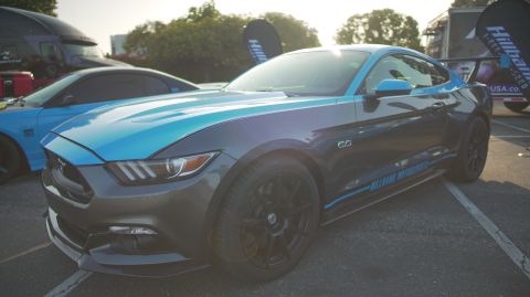1995 Ford Taurus - A modified Ford Mustang with racing stripes and a large rear spoiler is parked next to another car.