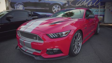 1995 Ford Taurus - A red Ford Mustang GT with silver racing stripes is parked at an outdoor event.