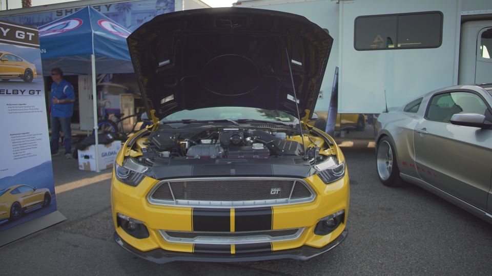 Yellow Mustang Shelby GT with hood open, showing engine. Another Mustang parked next to it