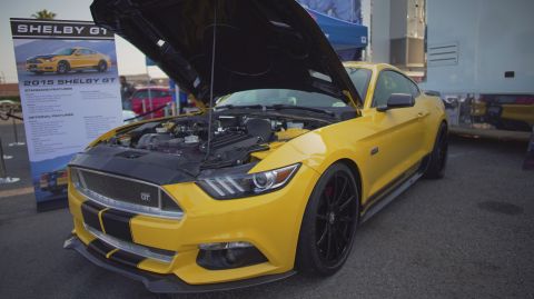 1995 Ford Taurus - A yellow 2015 Shelby GT Mustang is displayed with its hood open, revealing the engine and a prominent GT badge on the grille.