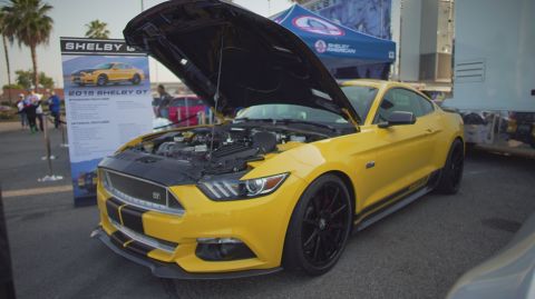1995 Ford Taurus - Yellow 2015 Shelby GT Mustang on display with its hood open, next to a promotional sign.