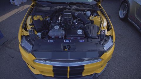 1995 Ford Taurus - The engine bay of a yellow Ford Mustang is open, revealing its supercharged engine and other components.