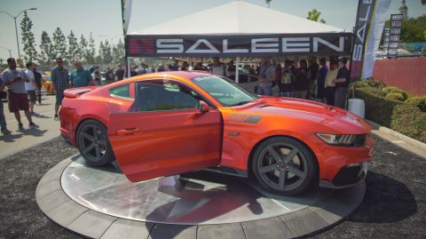 1995 Ford Taurus - An orange Saleen Mustang is displayed with its driver's door open on a turntable at an outdoor event.