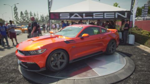 1995 Ford Taurus - An orange Saleen Mustang is displayed under a tent at an outdoor car show.
