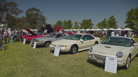 1995 Ford Taurus - Outdoor car show features multiple vehicles on display with spectators in the background.