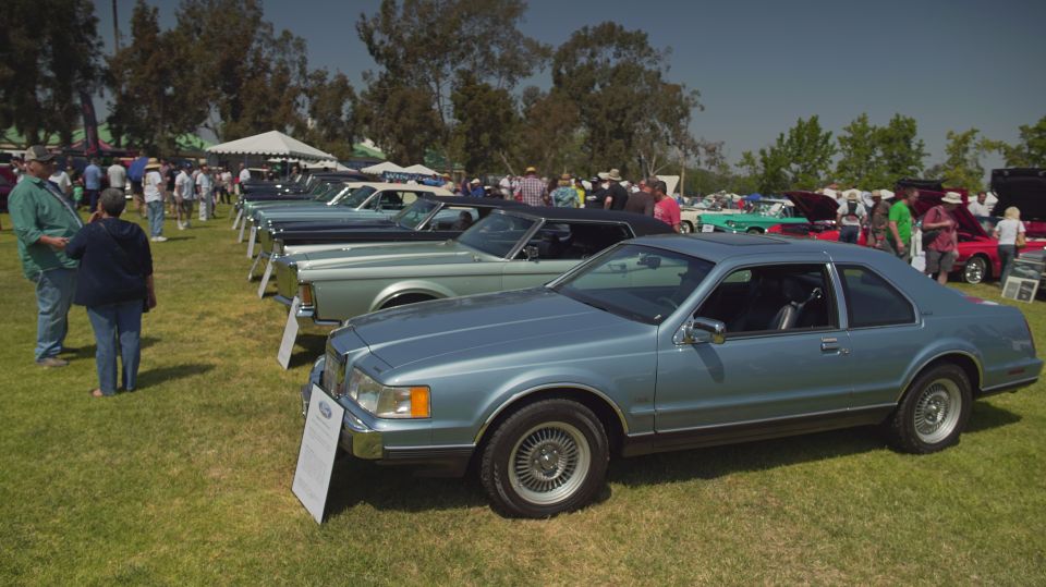 Light blue coupe with a vinyl roof parked on grass at a car show