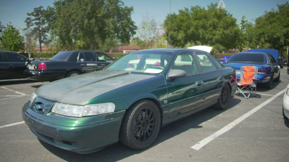 Green 1995 Ford Taurus sedan with a grey hood and black wheels