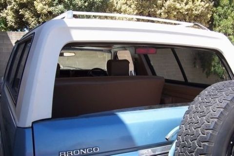 1985 Ford Bronco - Rear view of a blue and white Ford Bronco, showing its spare tire and roof rack.