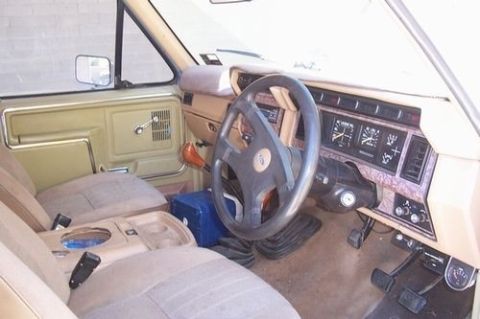 1985 Ford Bronco - The interior of a 1985 Ford Bronco features a tan dashboard with wood-grain accents and a prominent steering wheel.