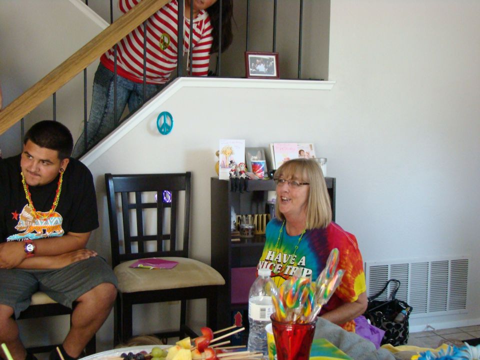 People gathered indoors, with a man in a black t-shirt and a woman in a tie-dye shirt