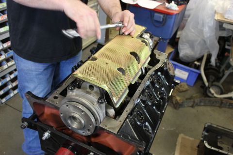 1979 Ford Bronco - Mechanic installs a yellow perforated cover onto an engine block during an engine build.