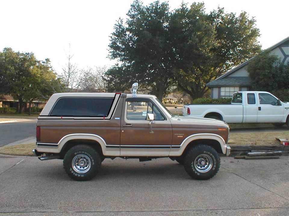 Brown and tan Ford Bronco with a camper shell, side view. Tires have white lettering