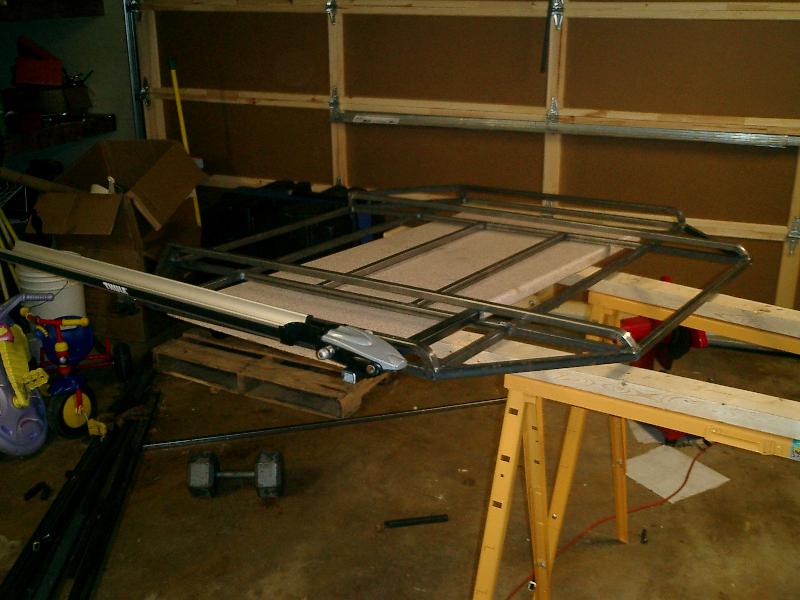 Metal rack assembly on sawhorses in a garage. Thule rack components visible