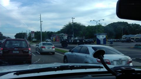 1994 Ford Bronco - Vehicles are stopped in traffic on a cloudy day, with buildings and trees lining the road.