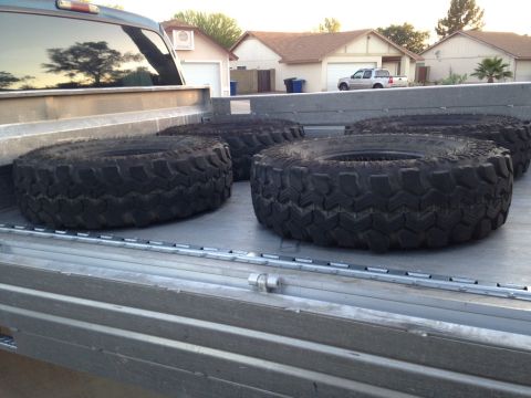 1987 Suzuki Samurai - Four large off-road tires are loaded into the bed of a pickup truck.
