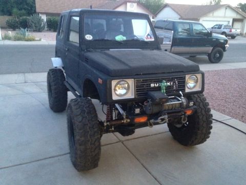 1987 Suzuki Samurai - Modified 1987 Suzuki Samurai with oversized tires and a front-mounted winch is parked on a driveway.