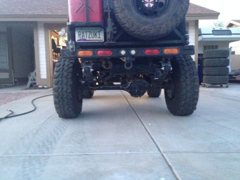 1987 Suzuki Samurai - The rear of a heavily modified off-road vehicle is shown, oversized tires and a custom license plate.