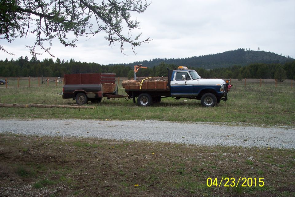 Side view of a 1973 Ford F-250 pickup truck towing a wood-laden trailer