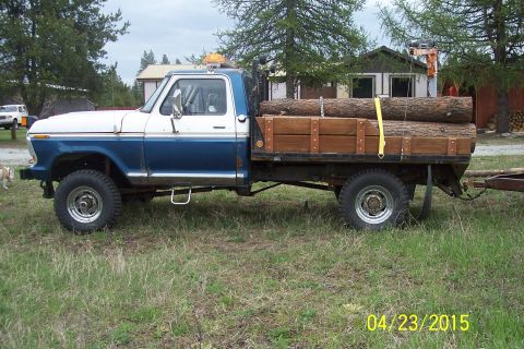 1973 Ford F-250 - A 1973 Ford F-250 flatbed truck is seen from the side, loaded with logs and hitched to a trailer.