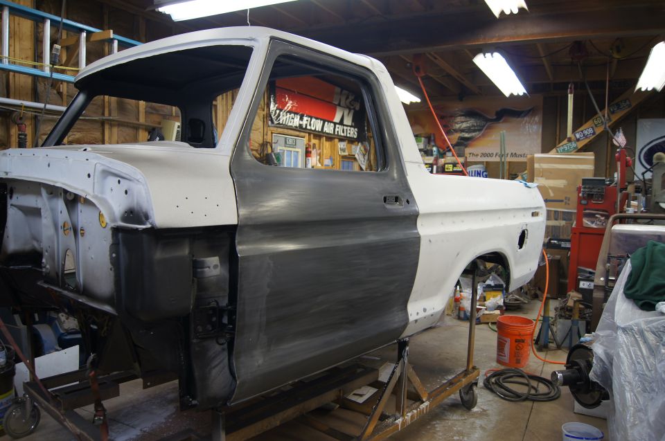 1979 Ford Bronco body undergoing restoration in a workshop, with primer and bare metal sections