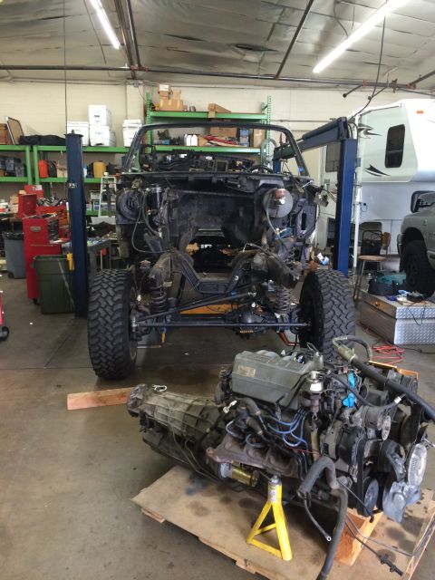 1992 Ford Bronco - A vehicle is disassembled in a garage with its engine and transmission removed and placed on the floor.