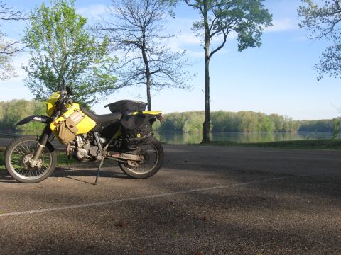 2006 Suzuki DR-Z400S - A yellow Suzuki motorcycle is parked on the side of a road next to a calm body of water with trees in the background.