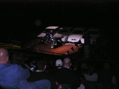 1996 Ford Bronco - A quad bike rider performs a stunt, leaping over a line of cars in a dark arena.