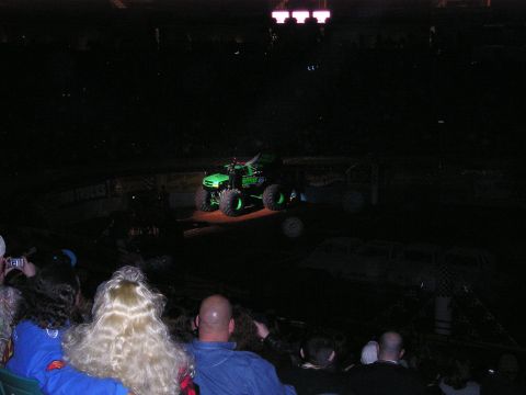 1996 Ford Bronco - A green monster truck is shown on a dirt arena with spectators in the foreground.