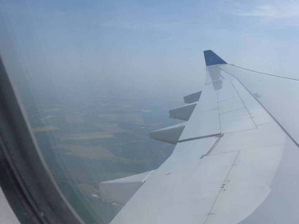 Airplane wing with blue tip seen from window, overlooking patchwork fields below