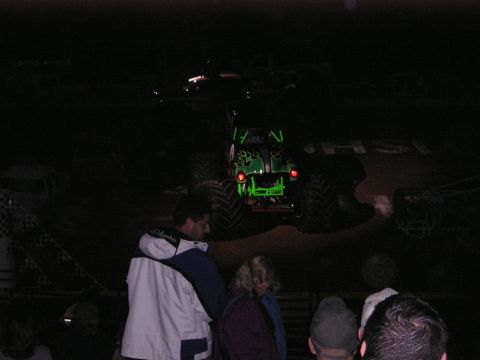 1996 Ford Bronco - A green monster truck is the focus of this nighttime scene, with spectators in the foreground.