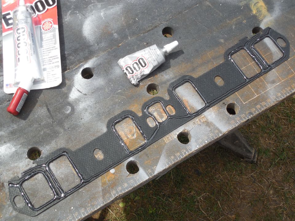Intake manifold gasket with sealant beads beside a tube of E6000 adhesive on a metal bench