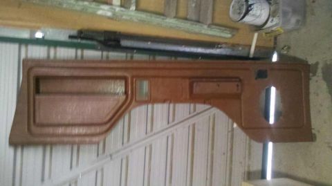 1982 Ford Bronco - A brown door panel, likely for a truck or SUV, is shown hanging against a wall. It features a large recessed area and a smaller storage com…