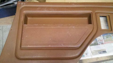 1982 Ford Bronco - Close-up of a brown interior door panel, likely from an older vehicle, showing a storage pocket and a cutout for a window crank.