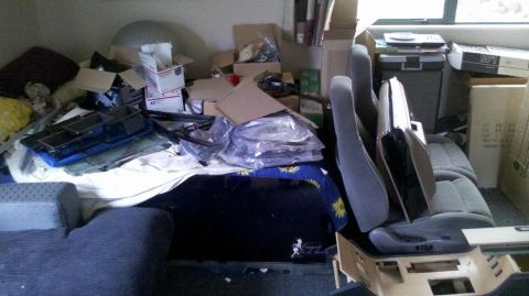 1982 Ford Bronco - A messy room filled with vehicle parts and storage boxes, including car seats and window components.