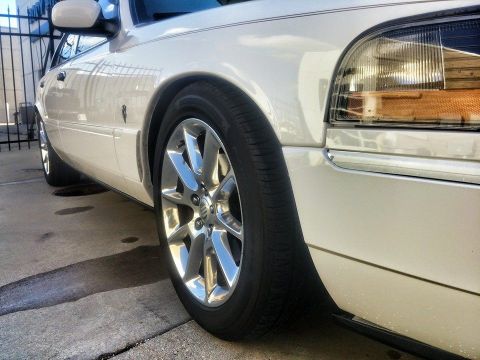 2000 Mercury Grand Marquis - A white sedan with a flat tire and chrome wheels is parked on a concrete surface.