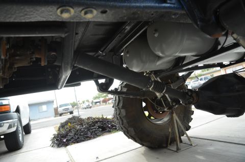 1979 Ford Bronco - Close-up view of the drive shaft and suspension components of a vehicle, with another truck partially visible.