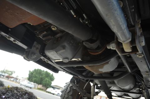 1979 Ford Bronco - Close-up of vehicle undercarriage, focusing on drive shaft and suspension components. Background shows a street scene.