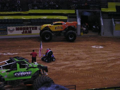 1996 Ford Bronco - Monster trucks are displayed in an arena, with a crowd visible in the background.