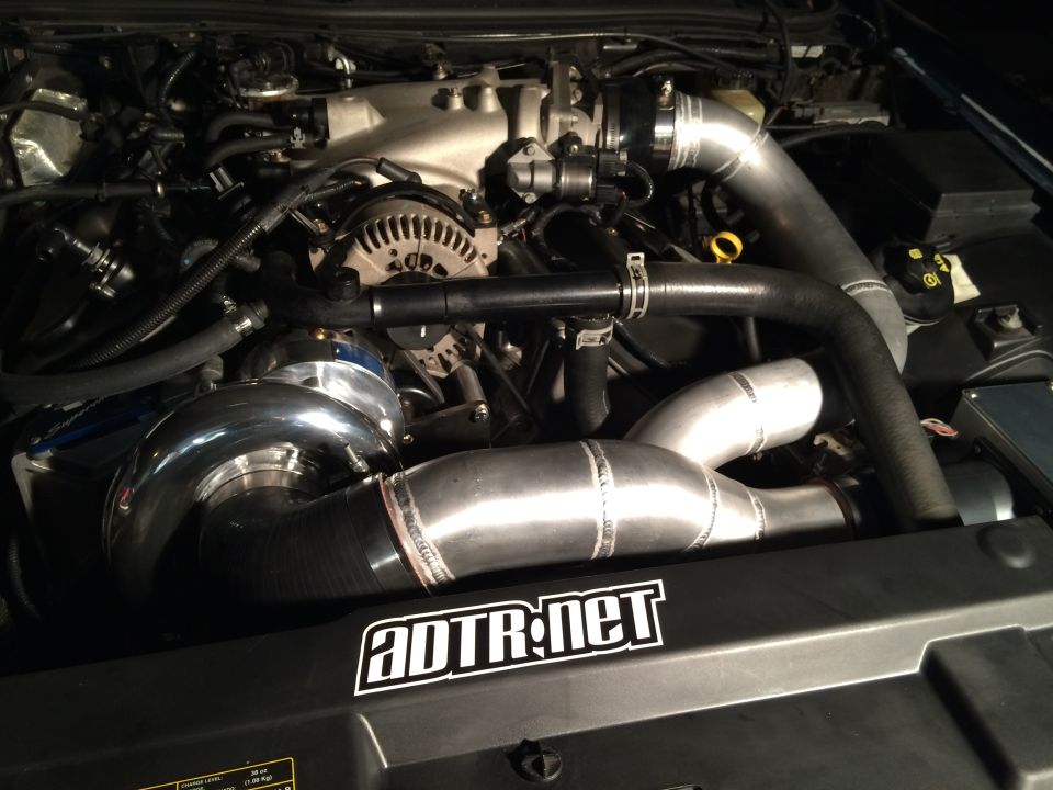 Engine bay with a polished supercharger and custom aluminum piping. ADTR.net sticker visible
