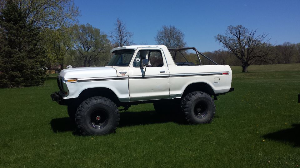 White lifted Ford Bronco with large tires parked on grass