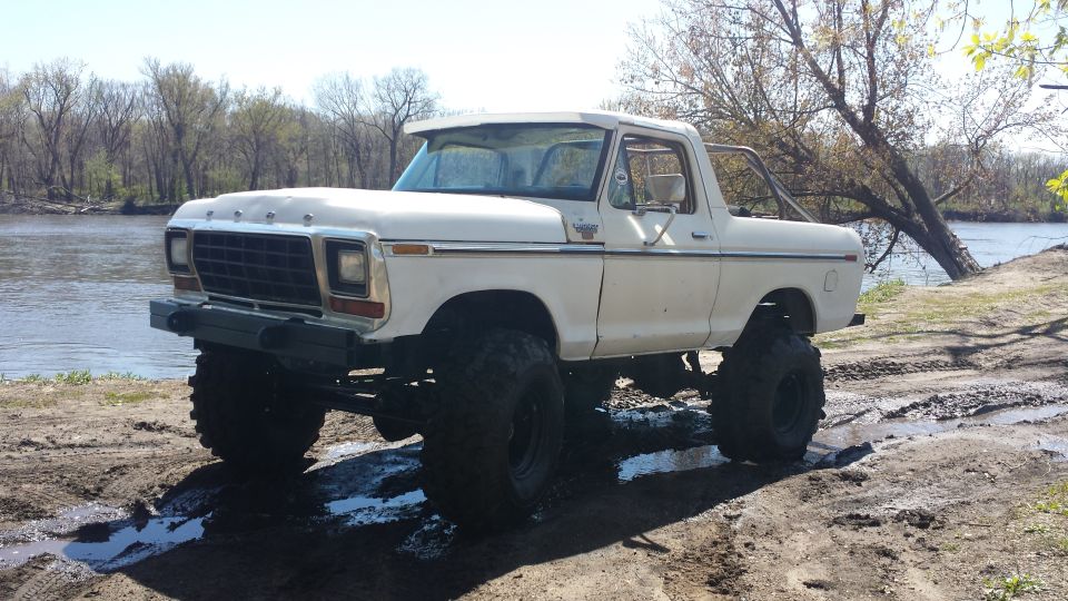 White 1979 Ford Bronco with large tires, lifted suspension, off-roading near a river