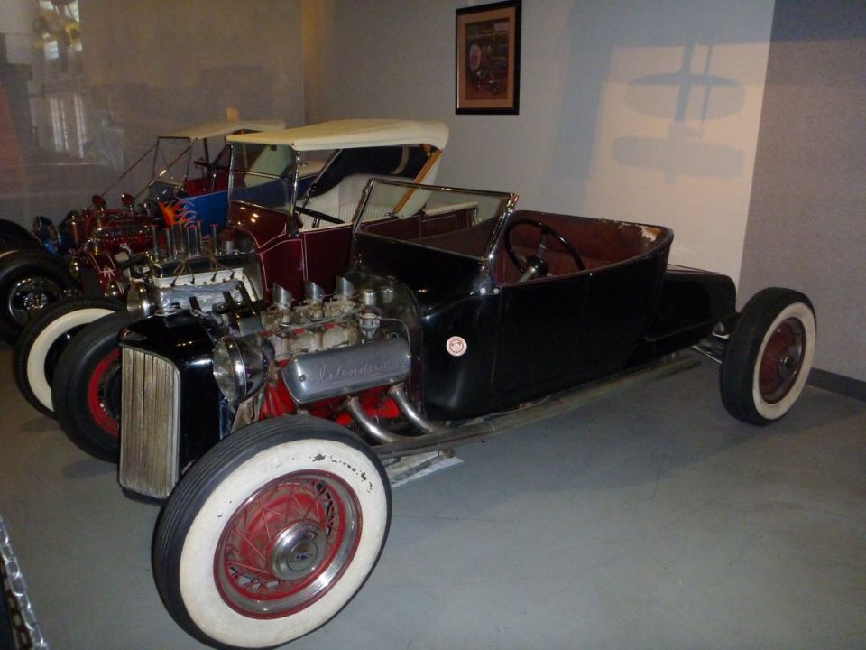 Black hot rod with exposed engine and whitewall tires, parked next to another hot rod