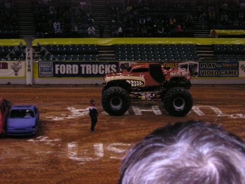 1996 Ford Bronco - A monster truck with a custom paint job sits on a dirt arena floor.